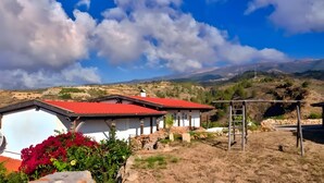 A rural house with a red roof, surrounded by a garden with red flowers, and a view of mountains in the background. - Holiday Apartment for 3 People (59 m²) in La Sabinita with Sea View (La Sabinita)