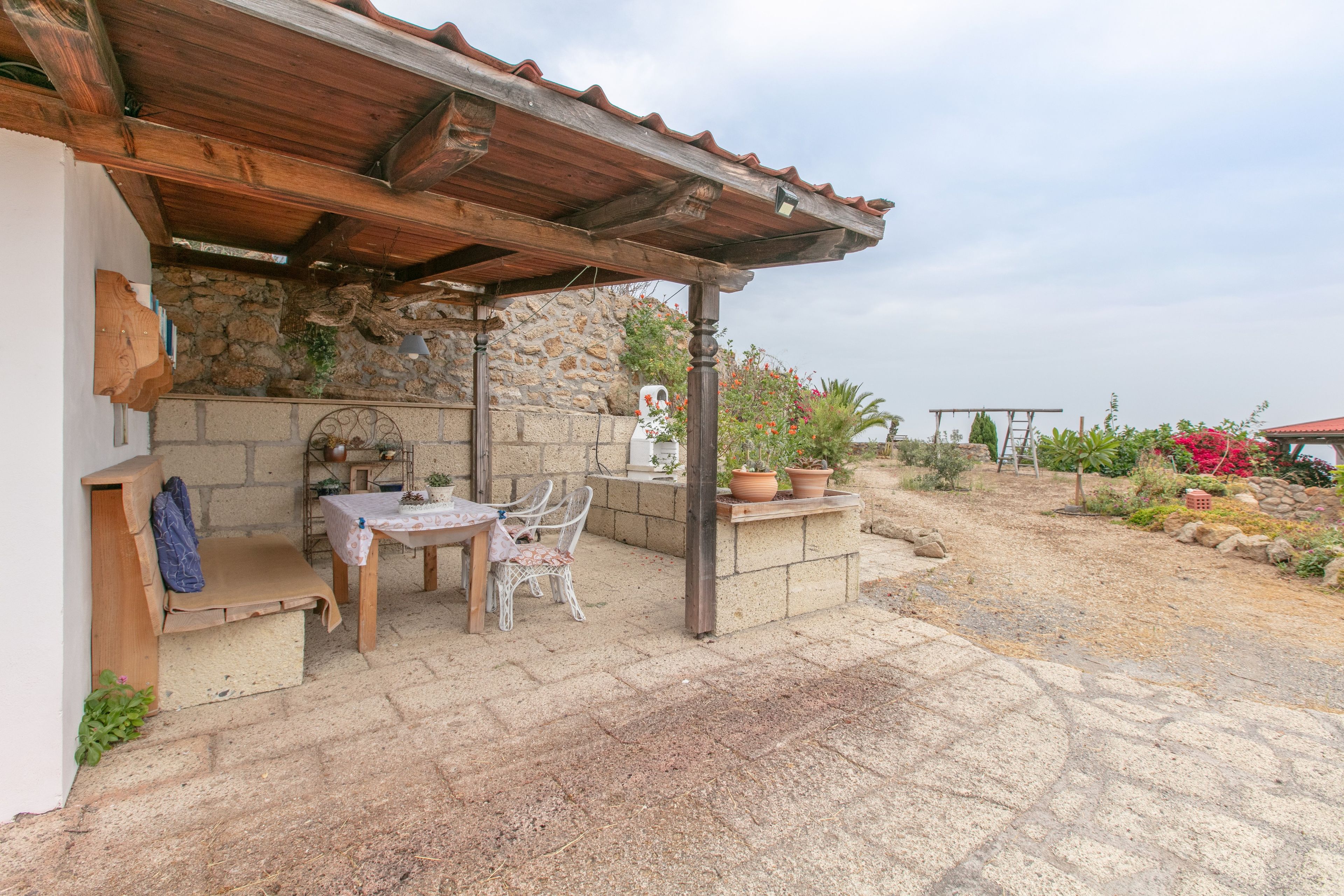 An outdoor patio with a stone wall, wooden furniture, and potted plants.