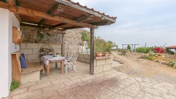 An outdoor patio with a stone wall, wooden furniture, and potted plants.