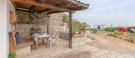 An outdoor patio with a stone wall, wooden furniture, and potted plants.
