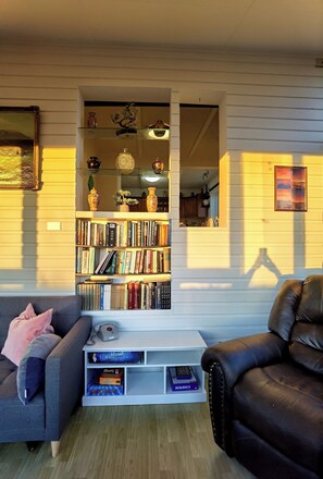 A living room with a bookshelf, two sofas, a coffee table, and a small kitchen visible through an open doorway.