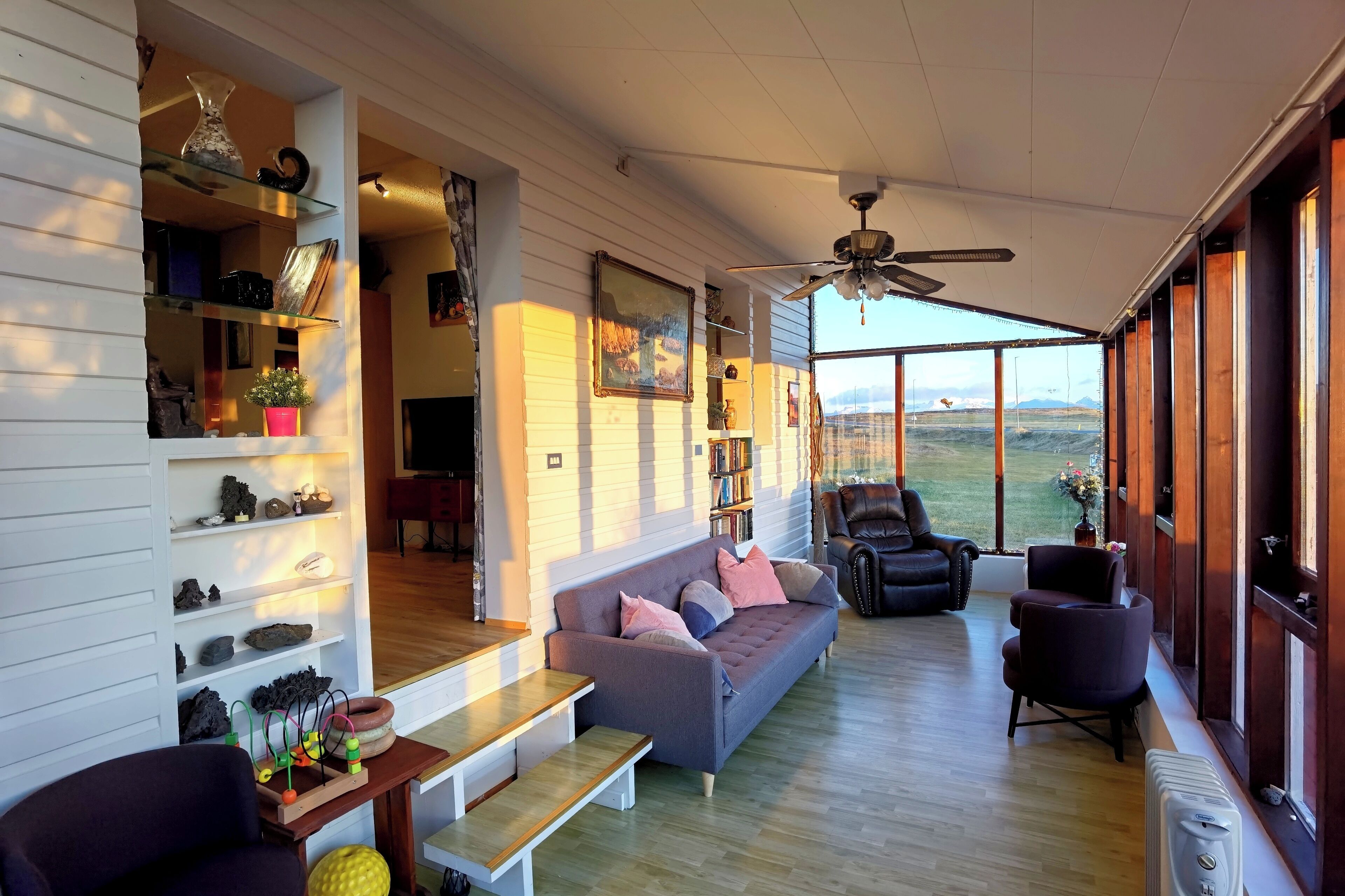 A spacious living area with a sofa, chairs, a wooden table, and a ceiling fan.