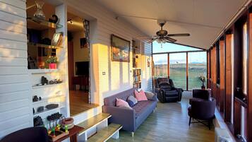 A spacious living area with a sofa, chairs, a wooden table, and a ceiling fan.