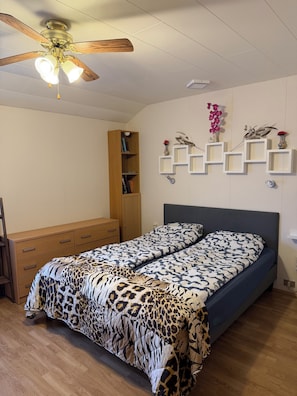 A bedroom with a bed, a wooden wardrobe, a ceiling fan, and wall-mounted shelves with decorative items. - Between the glacier and the ocean (Hellissandur)