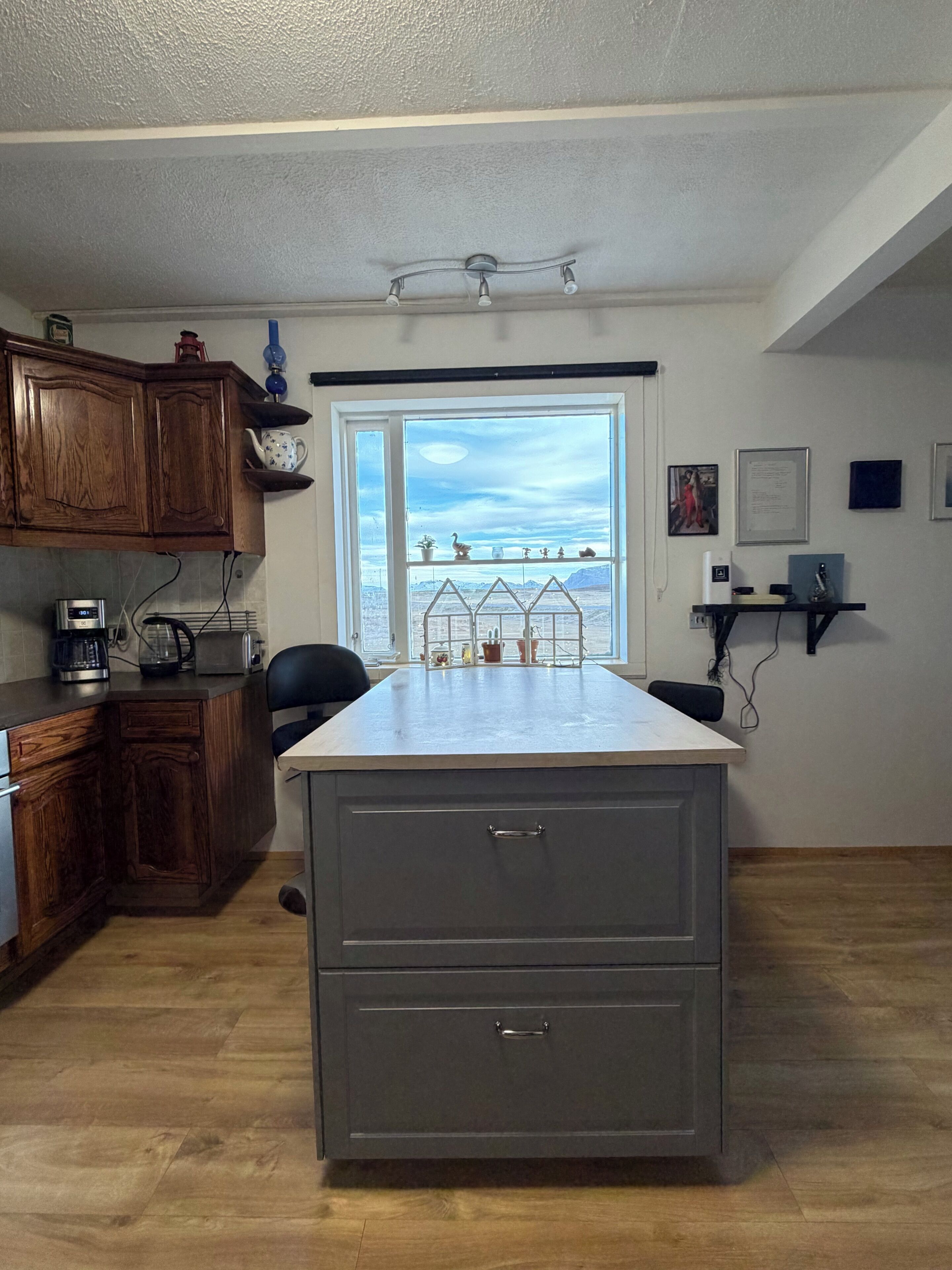 Una cocina con armarios de madera, una encimera, horno empotrado y ventana con vistas a un paisaje desértico.