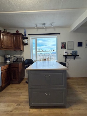 A kitchen with wooden cabinets, a countertop, a built-in oven, and a window with a view of a desert landscape.