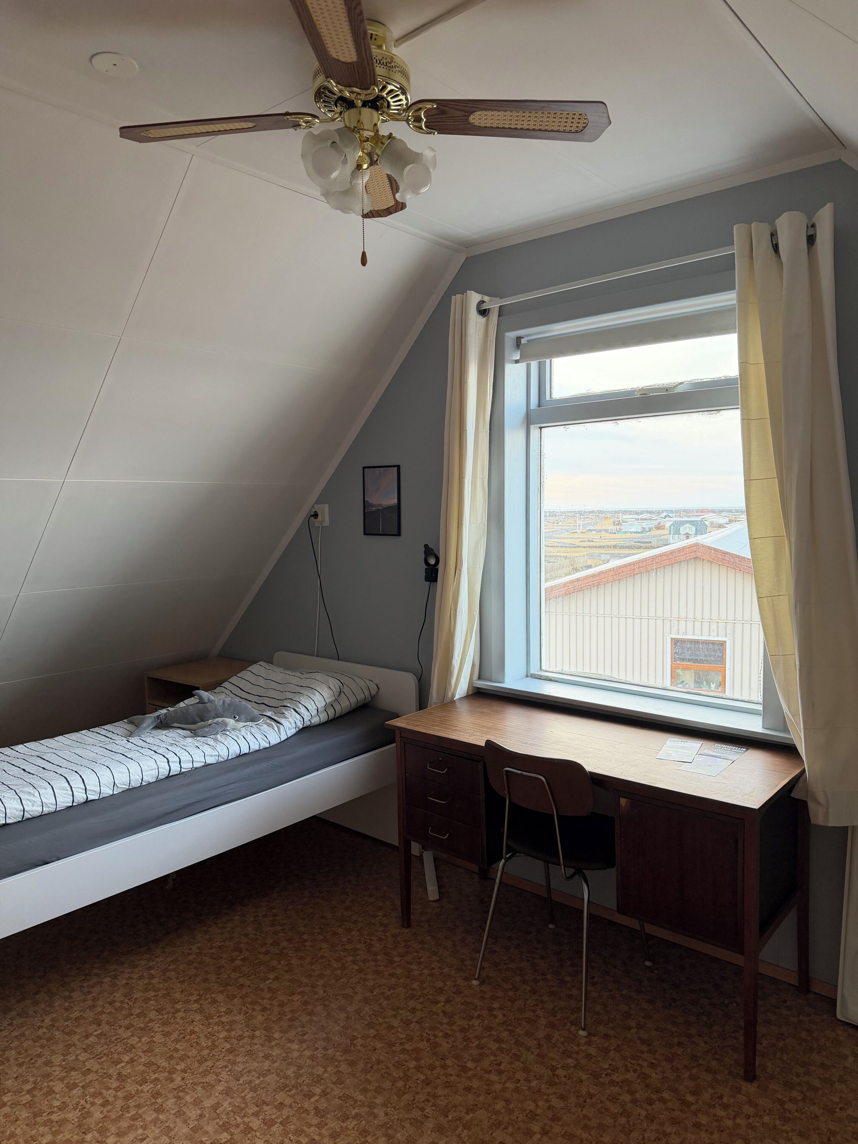 Una habitación tipo dormitorio con una cama, escritorio, silla y ventilador de techo.