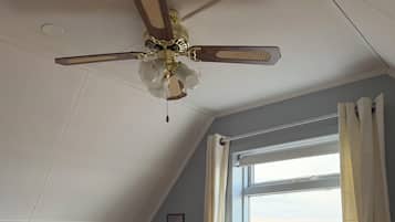 Una habitación tipo dormitorio con una cama, escritorio, silla y ventilador de techo.