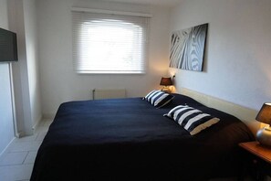 Un dormitorio con una cama grande, una ventana con persianas, una obra de arte en la pared y una lámpara de noche.