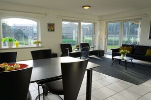 A modern living room with a dining area, large windows, and a view of the outside. - Residence Juliana 15 (Julianadorp)