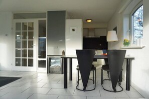 A modern kitchen with a dining area, featuring a black table and chairs, a window with a view, and a door leading to another room. - Residence Juliana 15 (Julianadorp)