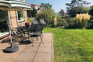 Un patio al aire libre con una mesa y sillas, rodeado de un césped cuidado y diversas plantas.