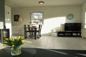A living room with a dining table, chairs, a TV, a clock, and a window. - Residence Juliana 15 (Julianadorp)