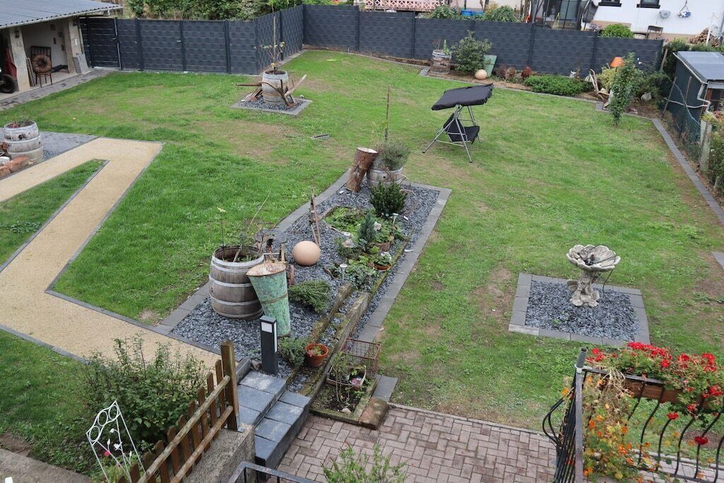 Een achtertuin met een terras, een vuurkuil, een bloembed en een kleine vijver.