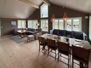 A spacious loft with a high ceiling, large windows, a dining area with a wooden table and chairs, and a cozy seating area with a sofa. - Mountain cabin on Glåmhaugen with terrace (Svingvold)