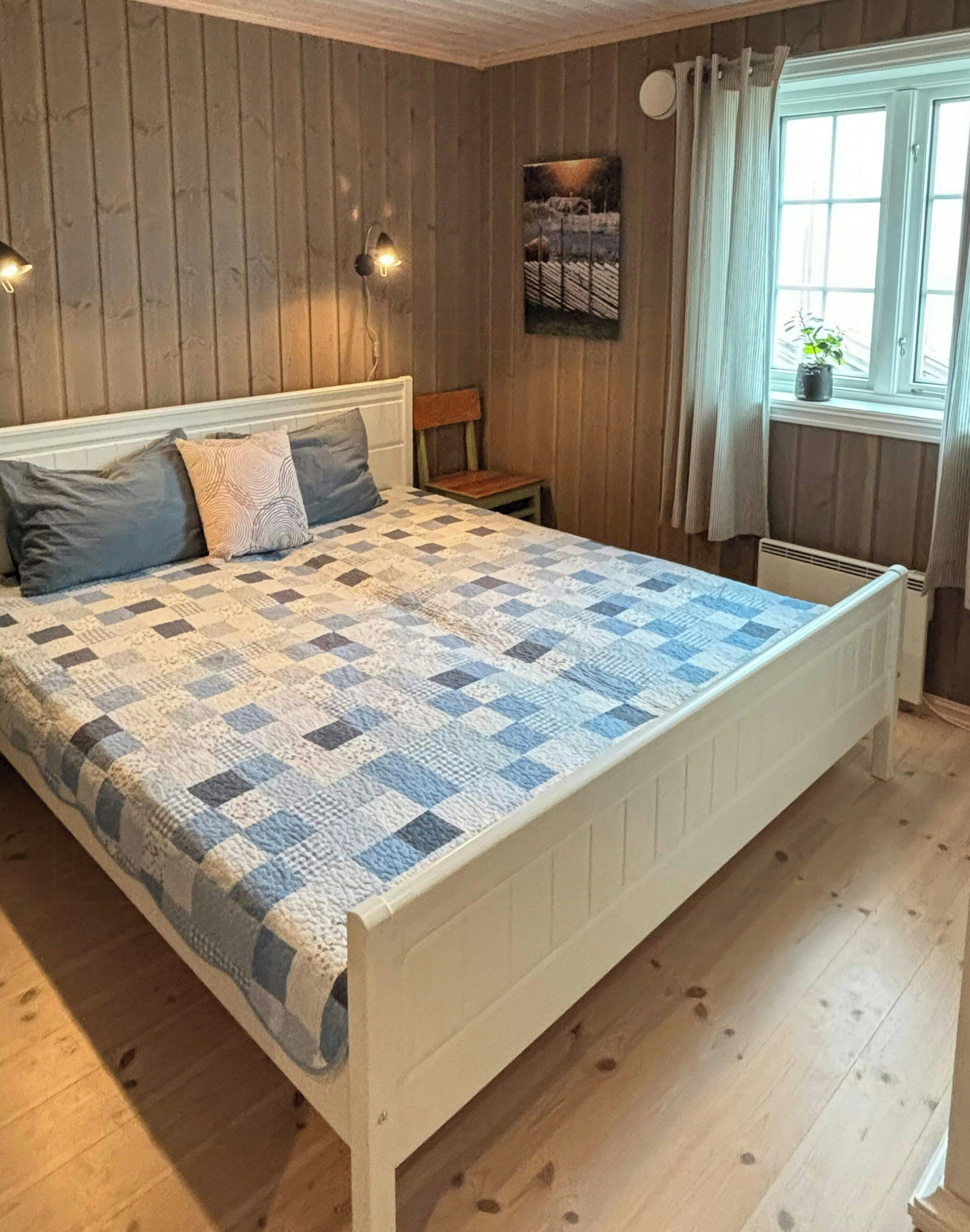 Makuuhuone, jossa on sänky, puupaneeliseinät, ikkuna verhoilla ja patteri.