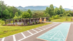 Una terraza con asientos al aire libre, una cancha de shuffleboard y vistas a montañas.