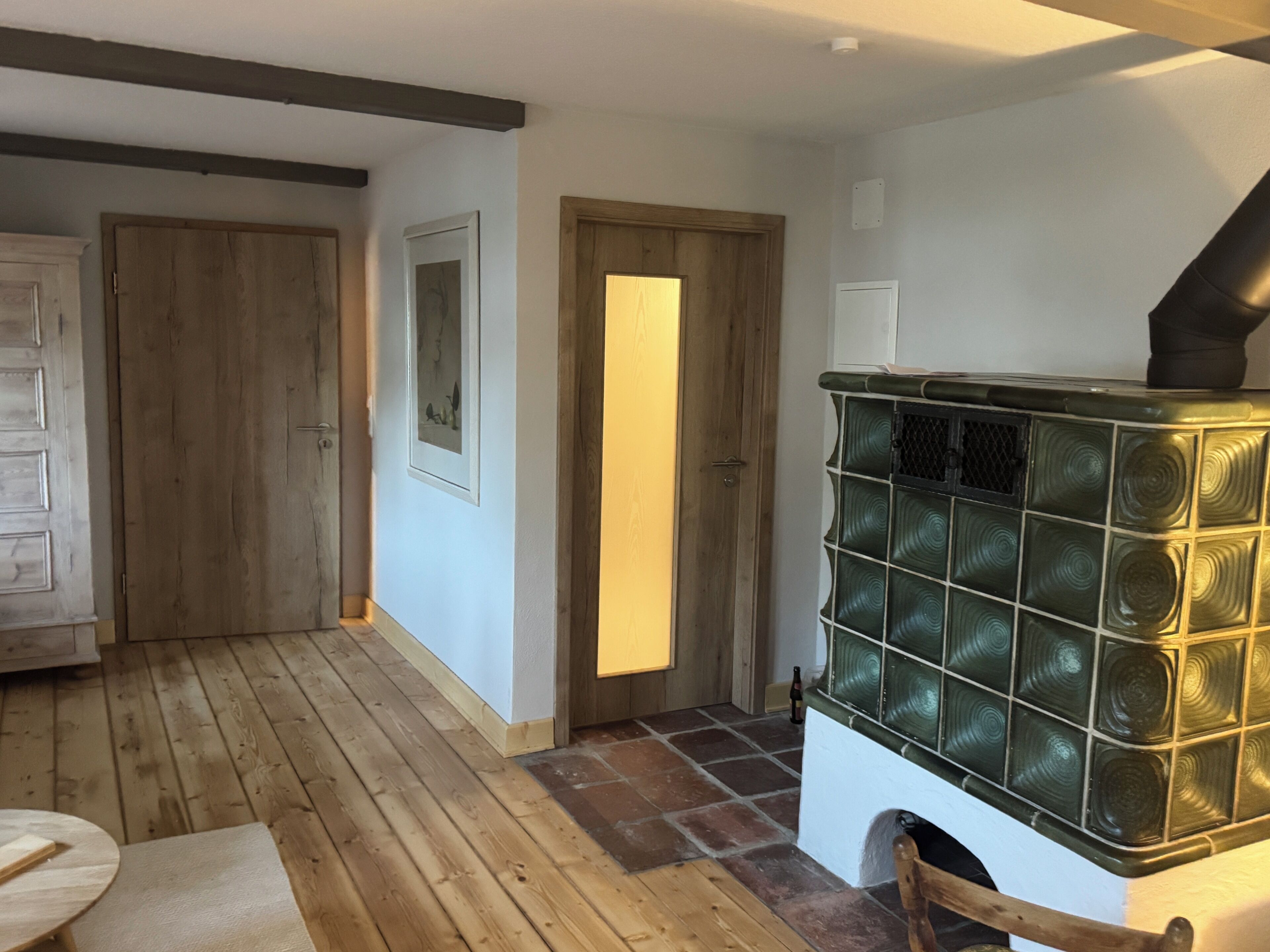 A room with a wooden floor, a fireplace with a glass front, and a door leading to another room.