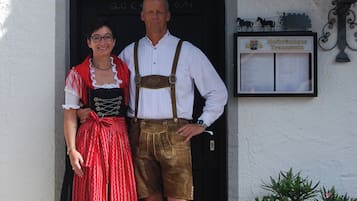 A man and woman in traditional attire standing in front of a building with a signboard.