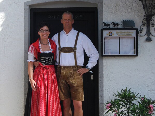 Un homme et une femme, vêtus de costumes traditionnels, se tiennent devant un bâtiment sur lequel on peut voir une enseigne.