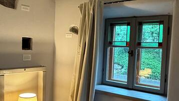 A room with a window, a lamp on a table, and a curtain.