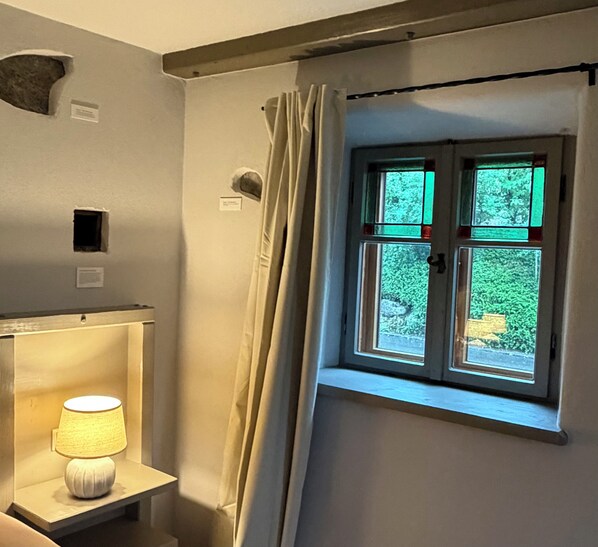 A room with a window, a lamp on a table, and a curtain.