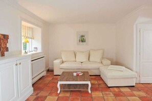 A living room with a white sofa, a wooden coffee table, and a radiator. - House on the Cliff - Weberhof (Keitum)