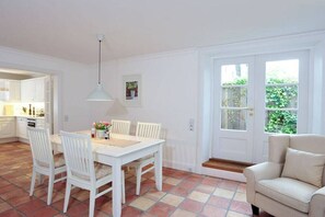 Ein Essbereich mit einem weißen Tisch und Stühlen, einer Pendelleuchte und Blick auf den Garten durch eine Tür.