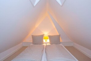 Ein kleines Schlafzimmer im Dachgeschoss, dreieckig, mit zwei Betten, einem Nachttisch und einer Lampe.