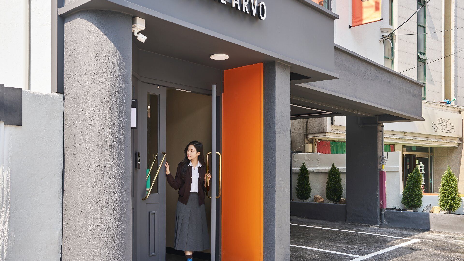 Entrada de hotel con diseño moderno, que incluye un puerta de cristal y un llamativo muro naranja.