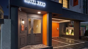 Een hotel ingang met een donkere gevel, een glazen deur en een bord boven de deur.