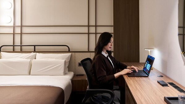 A hotel room with a bed, a desk, and a laptop.