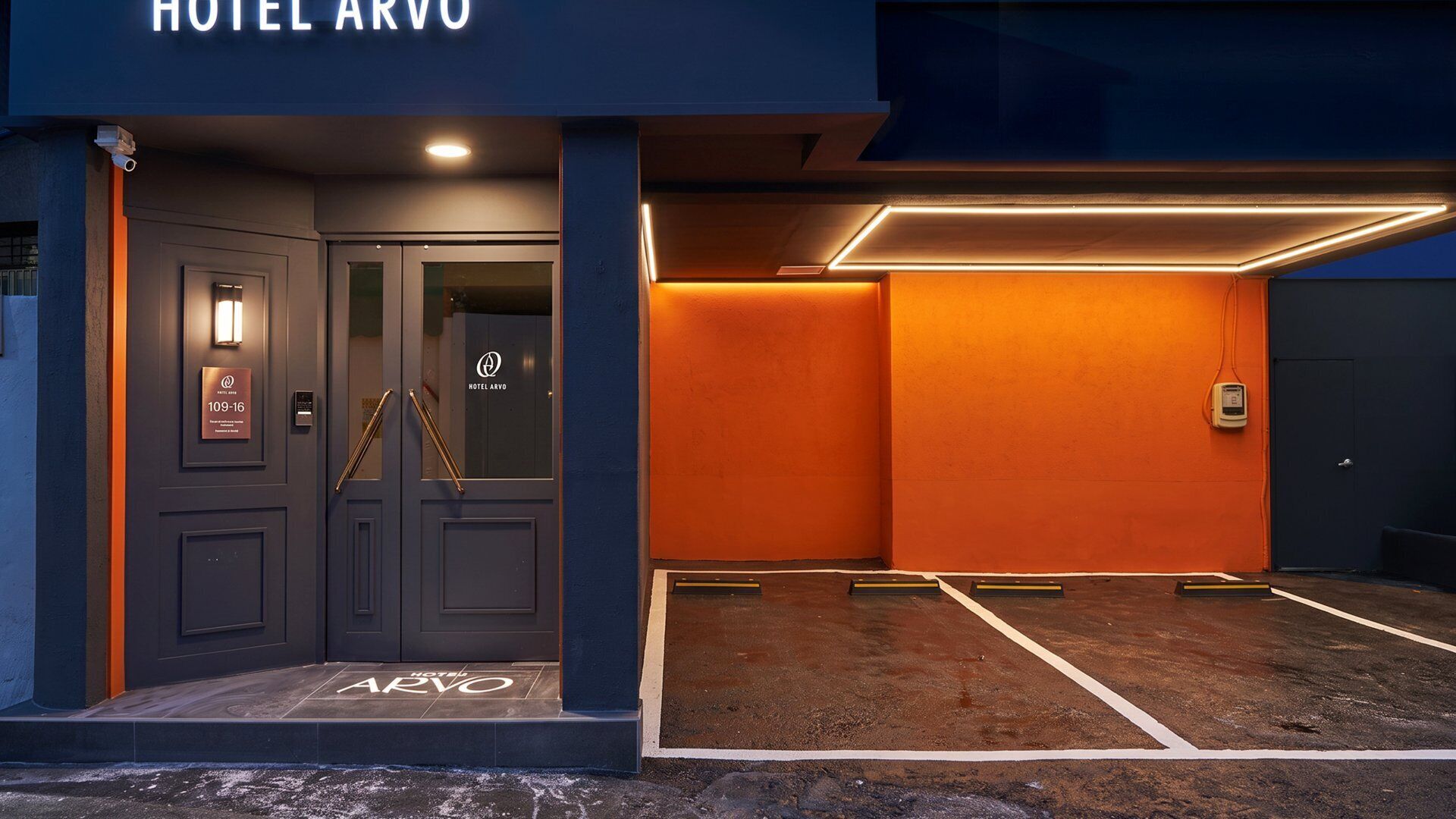 A hotel entrance with a dark facade, a glass door, and a sign indicating room number 109-16.