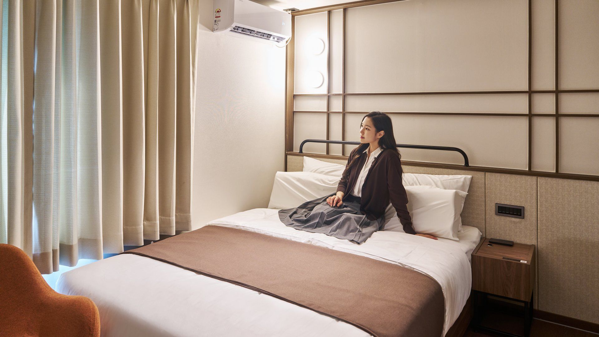 Ein Hotelzimmer mit Bett, Nachttisch, Stuhl und einem Vorhangfenster.