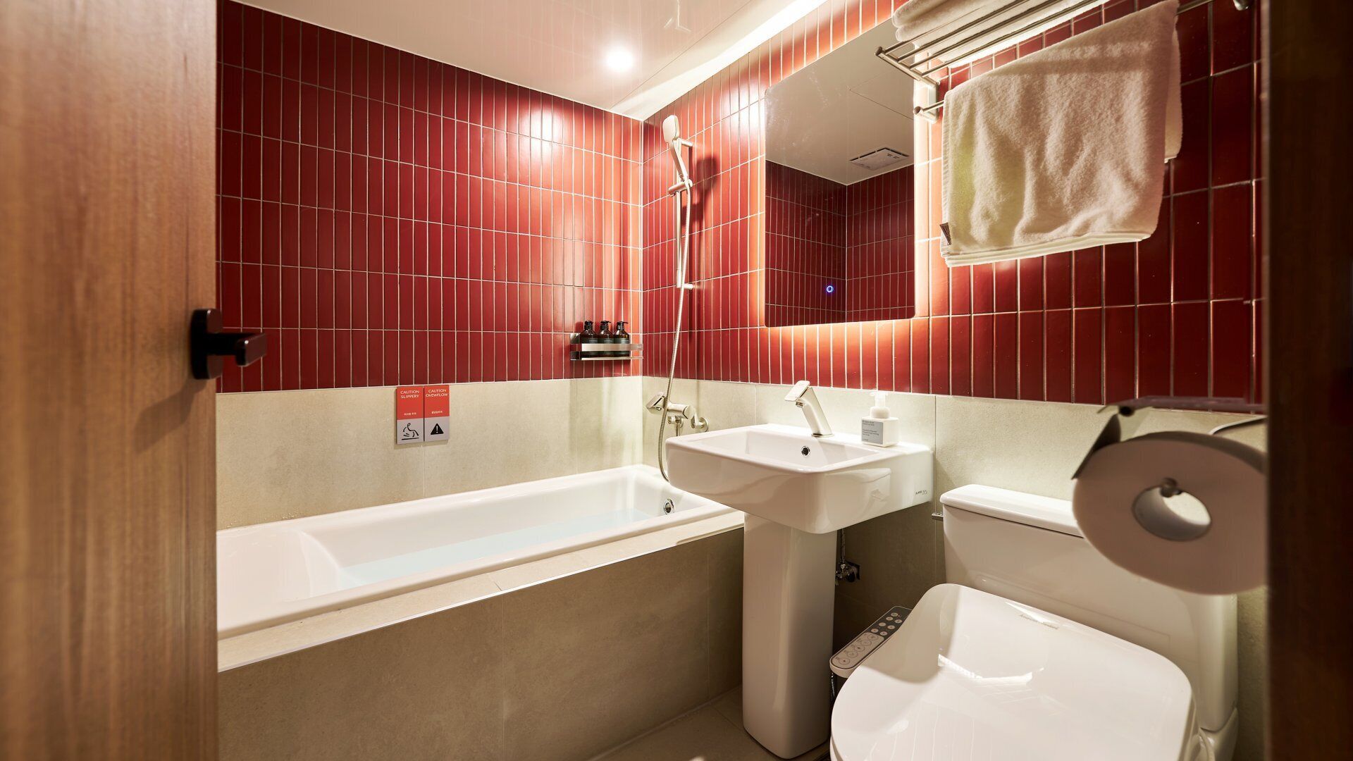 A bathroom with a bathtub, sink, and toilet. There is a towel rack above the sink and a caution sign on the wall.