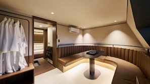Een moderne hotelkamer met zithoek, een tafel met glazen en een kledingkast met badjassen.