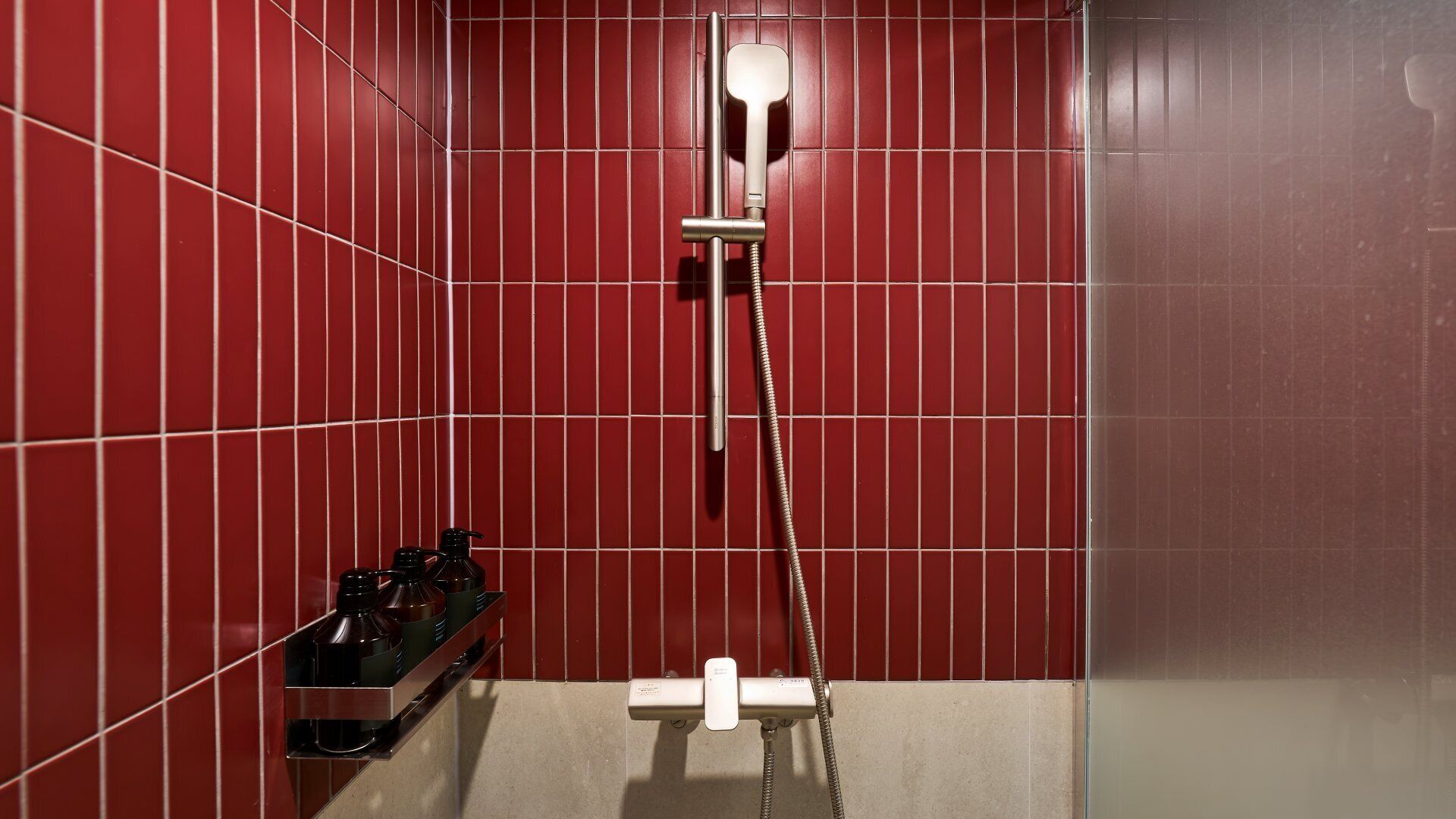 A red-tiled shower stall with a handheld showerhead and a wall-mounted faucet.