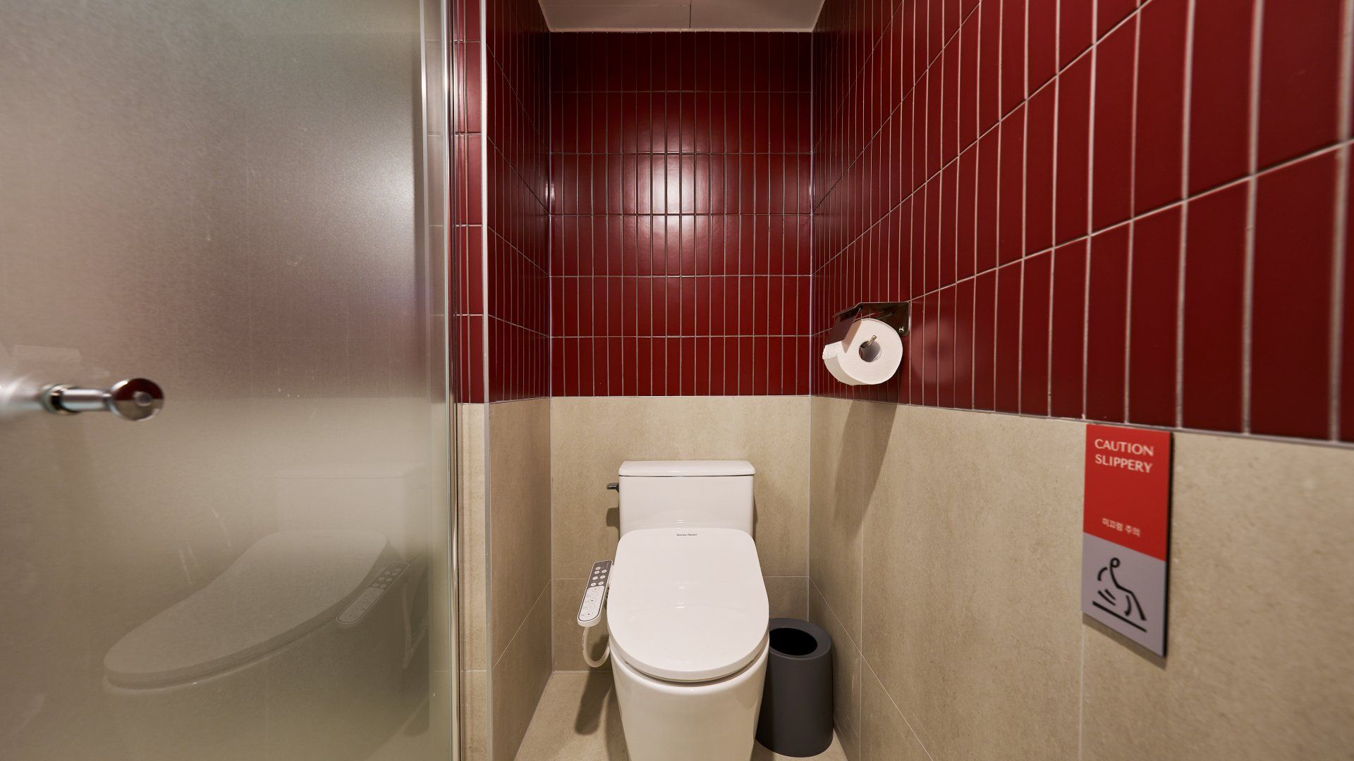 Une salle de bain équipée de toilettes, d’un sèche-mains et d’un panneau d’avertissement indiquant que le sol est glissant.