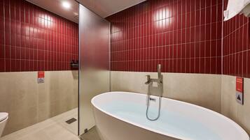 A bathroom with a freestanding bathtub, red tiled walls, and a glass shower enclosure.