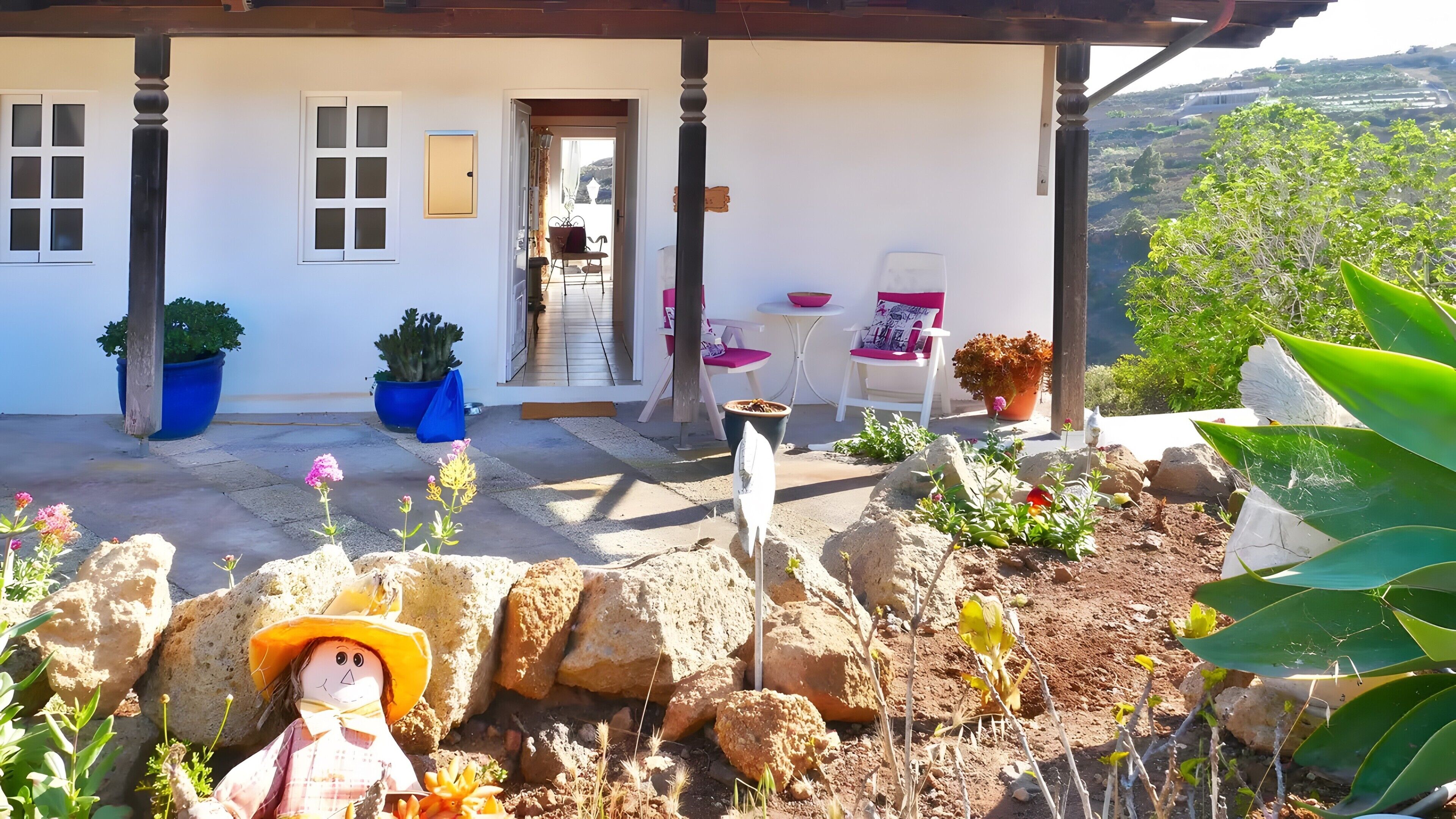 A house with a covered porch, potted plants, outdoor seating, and a view of the landscape.