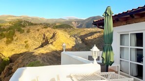Un balcó amb vista a un paisatge de muntanyes, una barana blanca i un parasol verd.