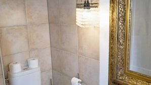 Ein Badezimmer mit beigen Fliesen, einer Toilette, einem Waschbecken und einem Spiegel mit aufwendigem Goldrahmen.