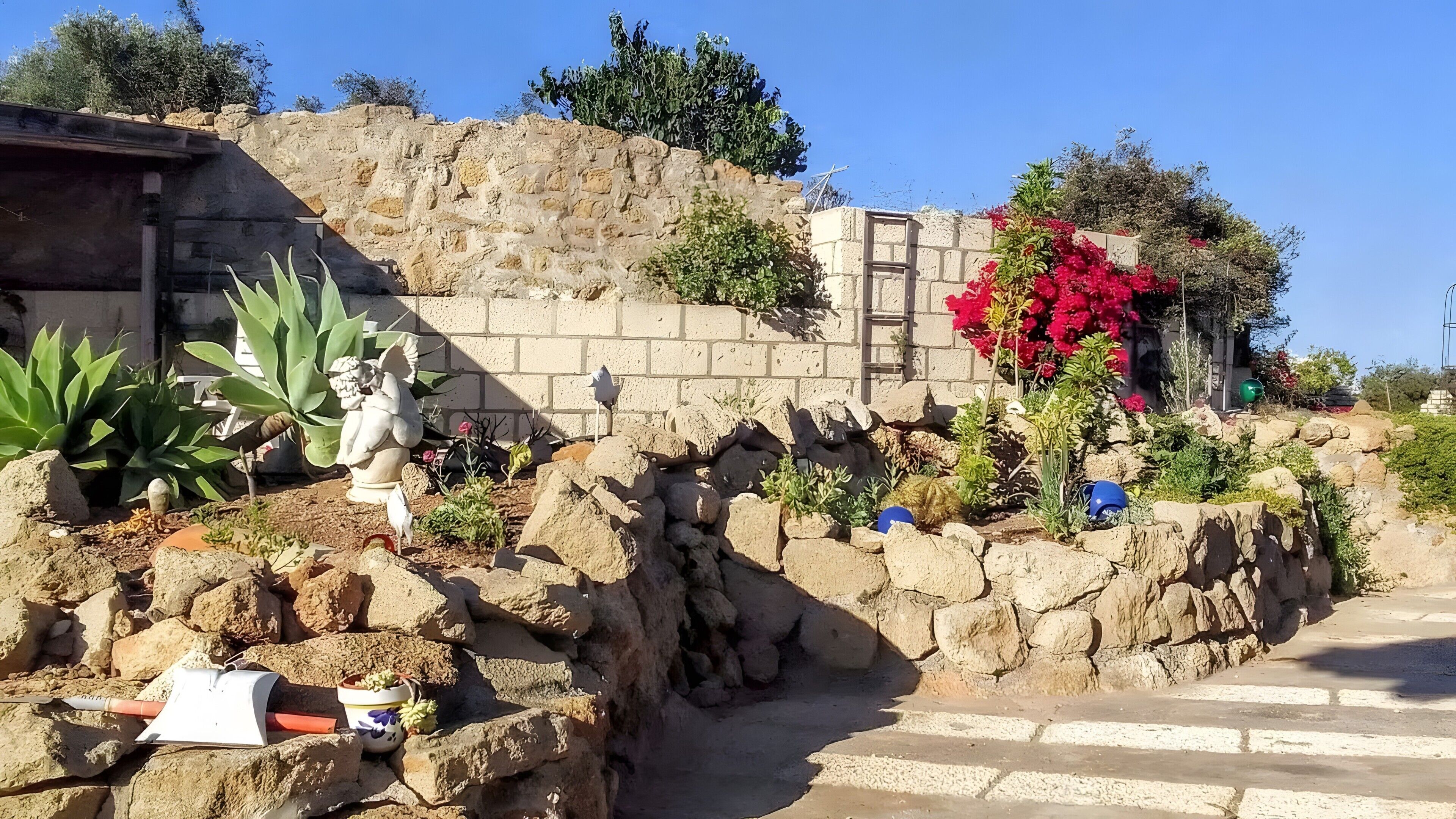 Ein Garten mit einer Statue, Steinen und Topfpflanzen.