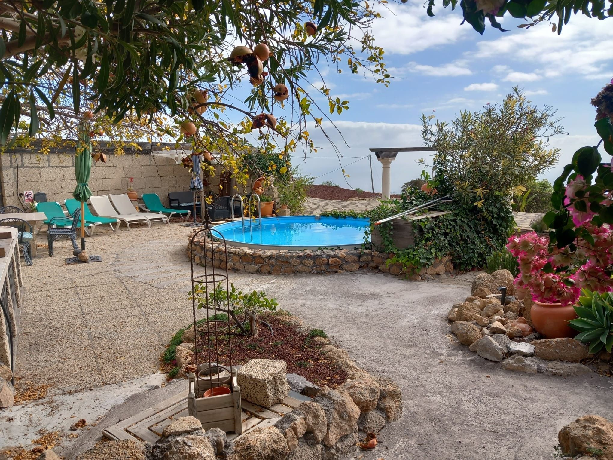 Un patio trasero con piscina, sillas de descanso y un muro de piedra.
