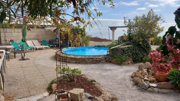 Un patio trasero con piscina, sillas de descanso y un muro de piedra.