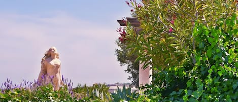A statue in a garden with various plants and a building in the background.
