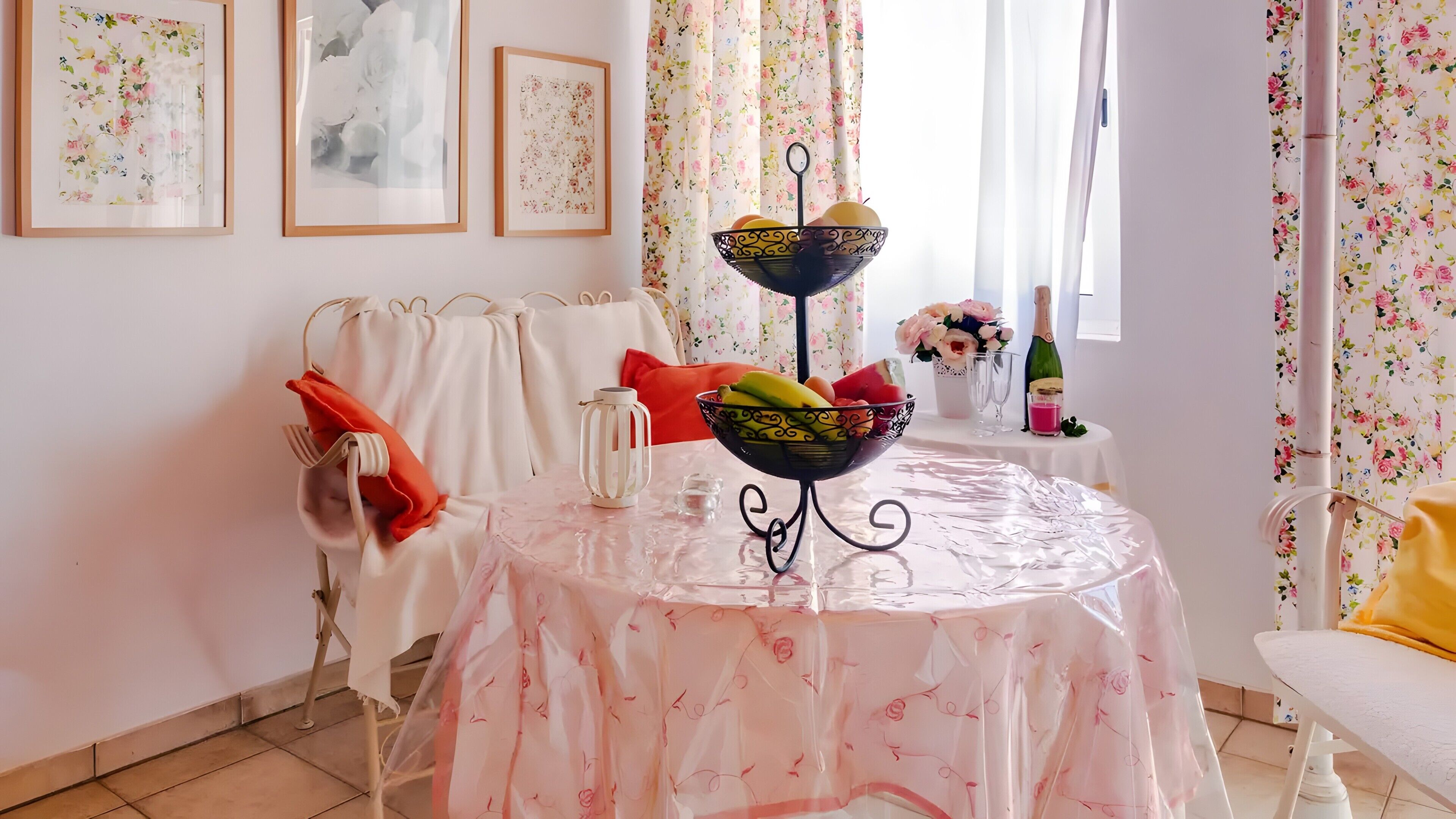 Un comedor con una mesa dispuesta para dos personas, con mantel floreado, frutero y una botella de champán.