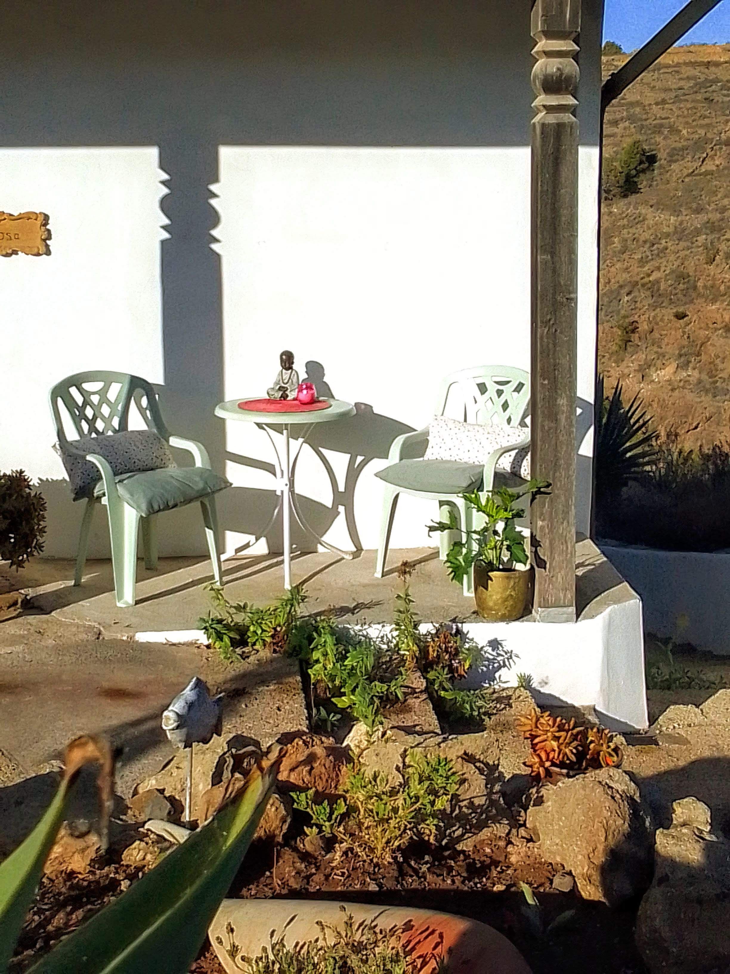 Een terras met een tafel en stoelen, omringd door potplanten en stenen.