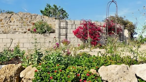 A garden with a stone wall, flowering plants, and a metal structure. - Casa Rosa – Charming Two-Bedroom Apartment with Panoramic Views (La Sabinita)