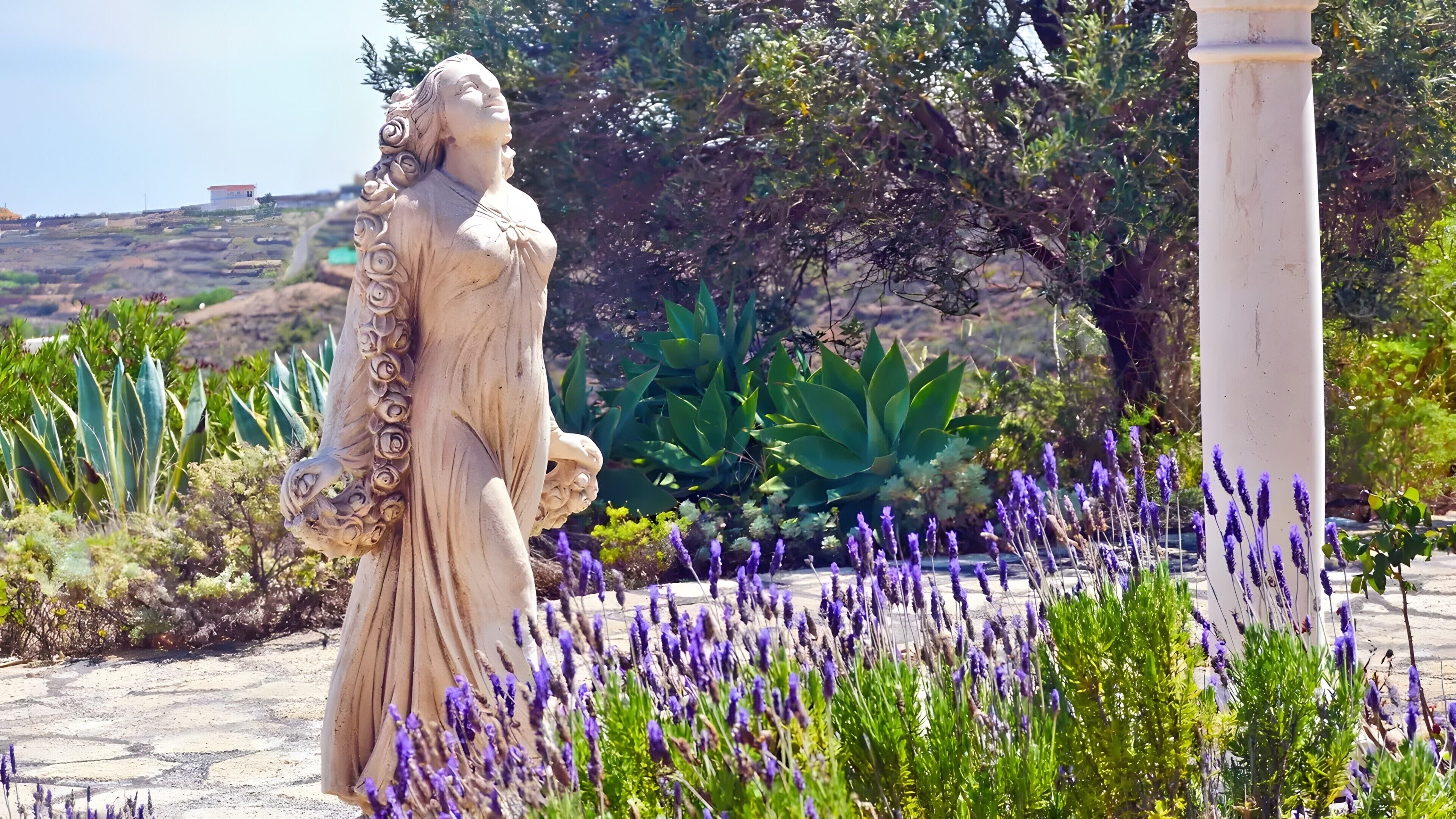 A statue in a garden with lavender and other plants.